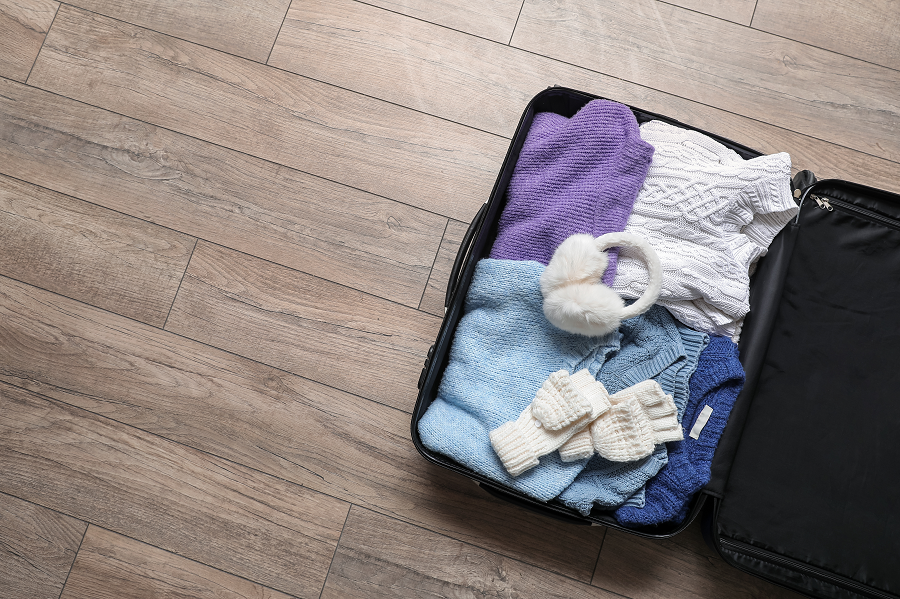 An open suitcase full of clothing suitable for a winter holiday, including knitted jumpers, ear muffs and a pair of gloves.